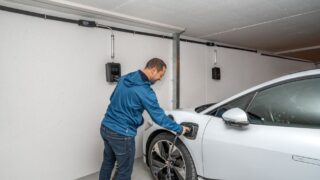 A man connects an electric car to a charging station in a modern indoor garage setting.
