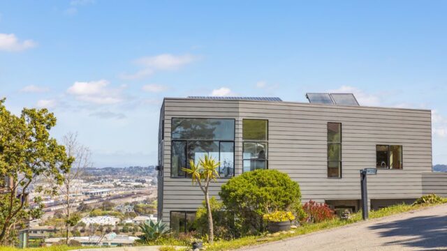 Contemporary hillside home with solar panels and city views on a clear summer day.