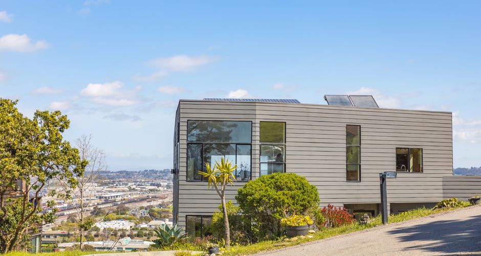 Contemporary hillside home with solar panels and city views on a clear summer day.