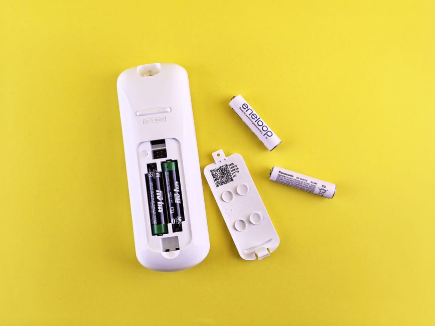Close-up of remote control and batteries on vibrant yellow surface.