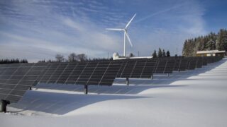 Solar panels and wind turbine in a snowy landscape, showcasing renewable energy sources.