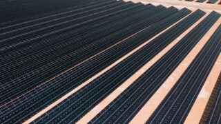 Aerial view of solar panels in a vast solar farm under bright sunlight.