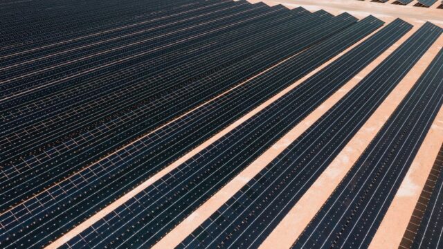 Aerial view of solar panels in a vast solar farm under bright sunlight.