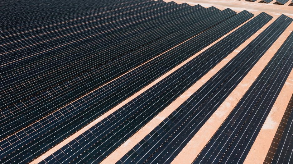 Aerial view of solar panels in a vast solar farm under bright sunlight.