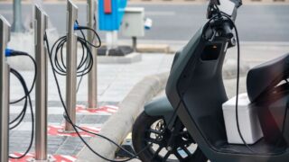 Electric scooter plugged into a charging station in a city environment, showcasing eco-friendly urban transportation.