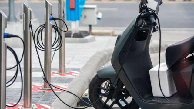 Electric scooter plugged into a charging station in a city environment, showcasing eco-friendly urban transportation.