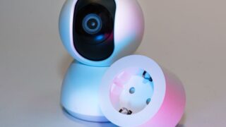 Smart home security camera and plug socket on a neutral background.
