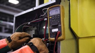 Electrician using a multimeter to fix industrial control panel wiring.