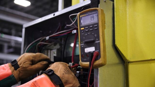 Electrician using a multimeter to fix industrial control panel wiring.