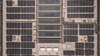 A high-angle drone shot capturing a grid of solar panels on a large industrial rooftop, showcasing renewable energy.