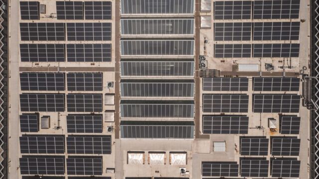 A high-angle drone shot capturing a grid of solar panels on a large industrial rooftop, showcasing renewable energy.