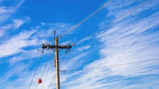 A wooden electrical pole with high voltage lines extending into a vivid blue sky with scattered clouds.
