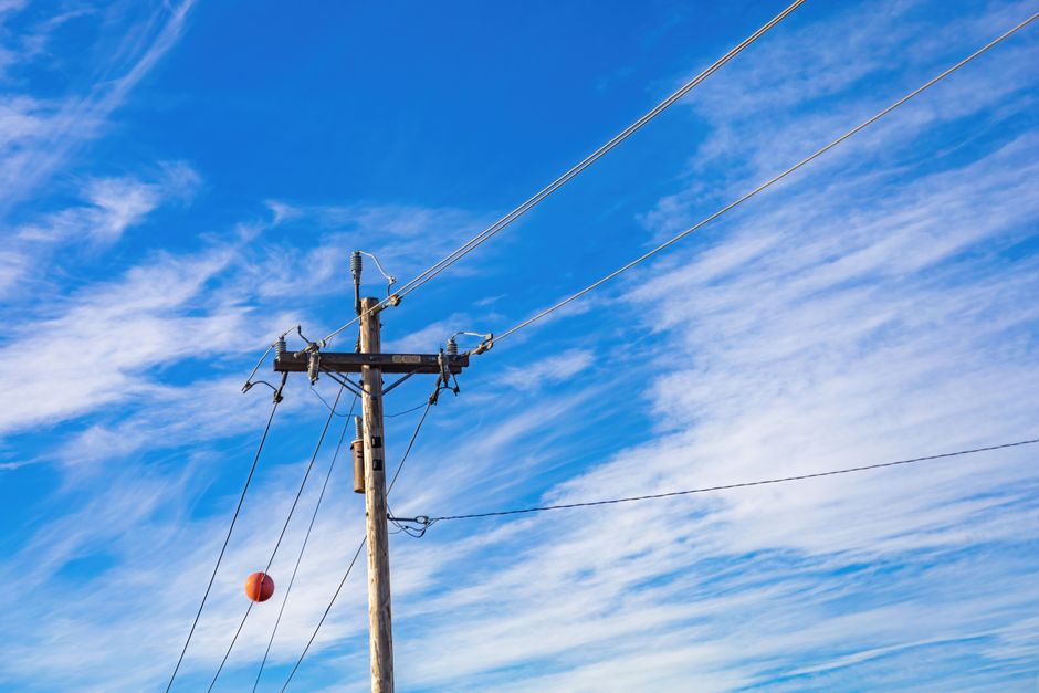 A wooden electrical pole with high voltage lines extending into a vivid blue sky with scattered clouds.
