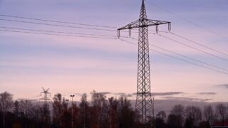Scenic view of a high voltage transmission tower against a sunset sky, surrounded by autumn trees.