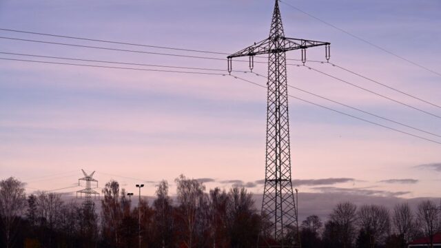 Scenic view of a high voltage transmission tower against a sunset sky, surrounded by autumn trees.