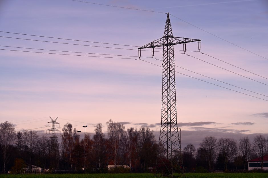 Scenic view of a high voltage transmission tower against a sunset sky, surrounded by autumn trees.