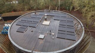 Overhead shot of rooftop solar panels on a circular building in a wooded area.