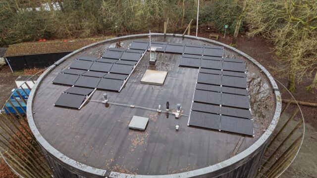 Overhead shot of rooftop solar panels on a circular building in a wooded area.