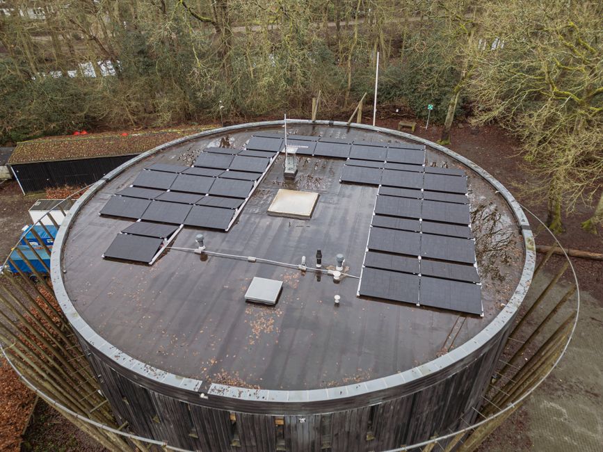 Overhead shot of rooftop solar panels on a circular building in a wooded area.