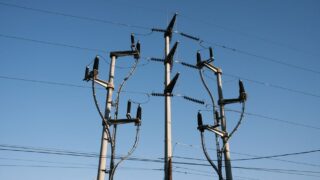 High-voltage power lines and poles silhouetted against a clear blue sky, representing energy distribution.