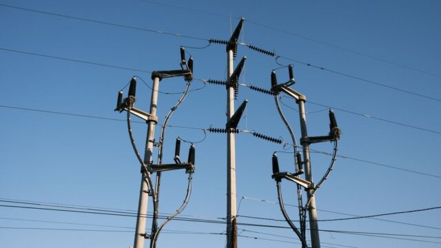 High-voltage power lines and poles silhouetted against a clear blue sky, representing energy distribution.