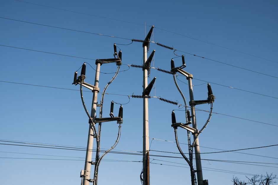 High-voltage power lines and poles silhouetted against a clear blue sky, representing energy distribution.