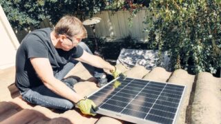 Male technician installing solar panel on roof, promoting sustainable energy.