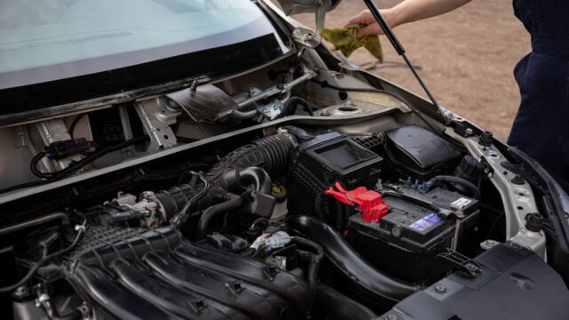 Mechanic inspecting car engine bay and battery during routine maintenance.