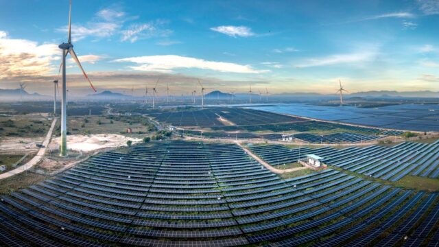 Panoramic aerial view of a renewable energy farm with solar panels and wind turbines in Vietnam at sunset.