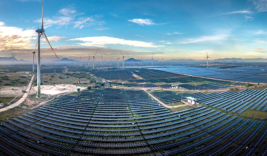Panoramic aerial view of a renewable energy farm with solar panels and wind turbines in Vietnam at sunset.