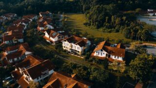 Aerial view of suburban houses with red roofs surrounded by greenery at sunset.
