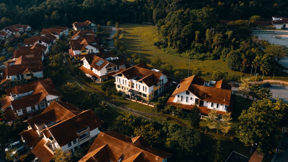 Aerial view of suburban houses with red roofs surrounded by greenery at sunset.
