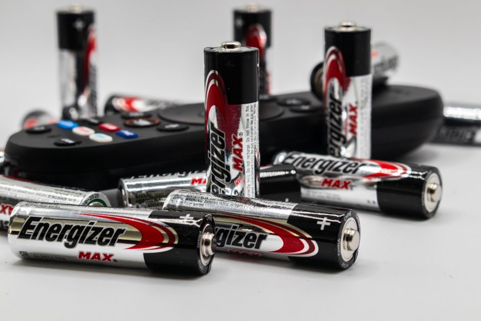 Close-up of multiple Energizer AA batteries and a remote control on a white surface.