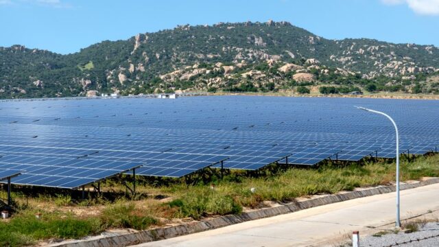 A vast solar farm set against a mountainous landscape under a blue sky.