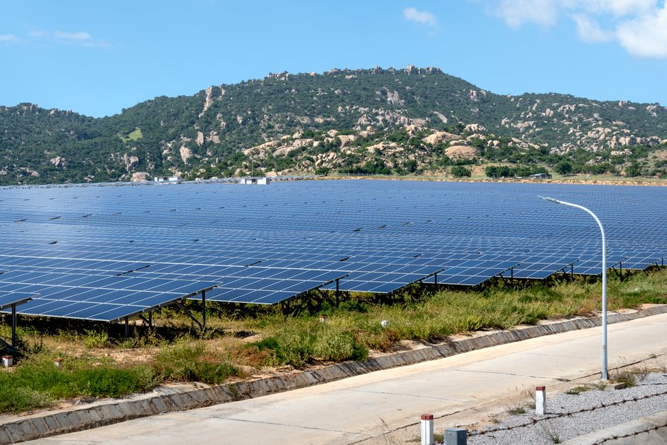 A vast solar farm set against a mountainous landscape under a blue sky.