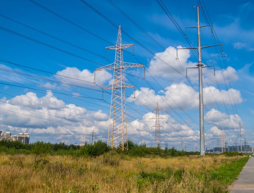 High voltage power lines stretching across a grassy field under bright blue skies with clouds.