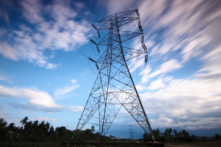 Dramatic view of a high voltage transmission tower set against a dynamic cloudy sky, showcasing modern energy infrastructure.
