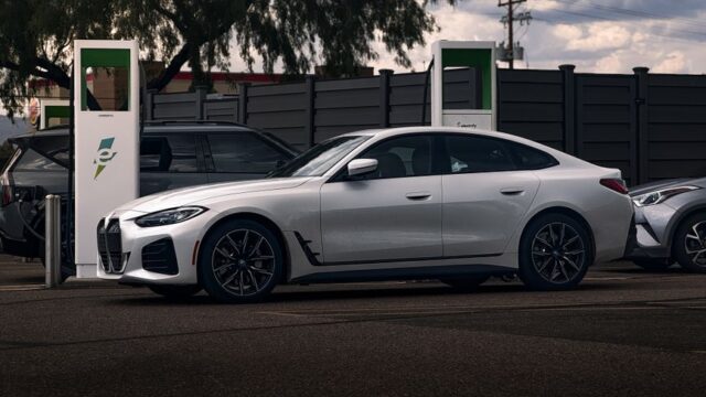 A sleek white coupe parked at an electric charging station outdoors on a cloudy day.