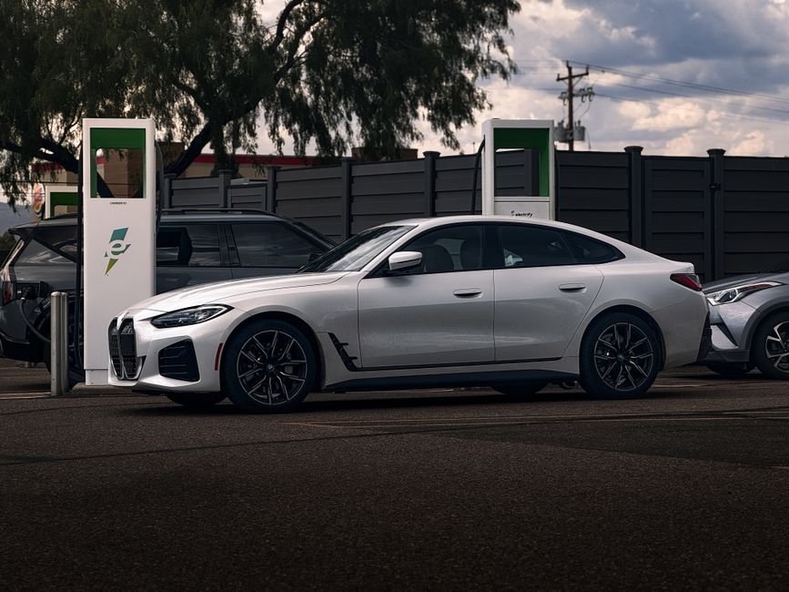 A sleek white coupe parked at an electric charging station outdoors on a cloudy day.