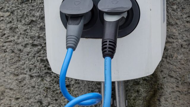 Close-up of an electric vehicle charging station with two cables in sockets against a textured wall.