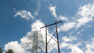 High-voltage power lines and towers set against a vibrant blue sky with scattered clouds.