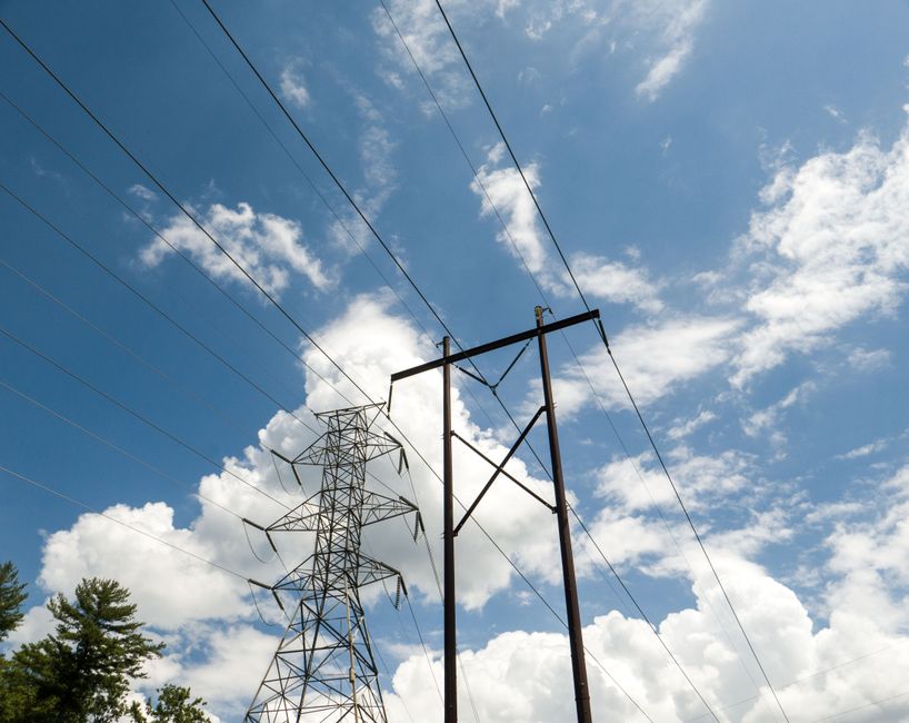 High-voltage power lines and towers set against a vibrant blue sky with scattered clouds.
