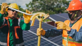 Two construction workers assembling solar panel equipment under sunny conditions, showcasing teamwork and renewable energy.