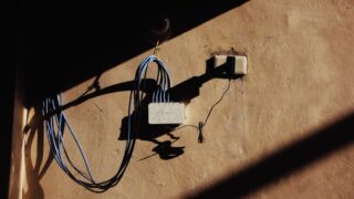 Electric blue wires connected to network adapter plugged in socket on shabby brown wall of building on street with shadow