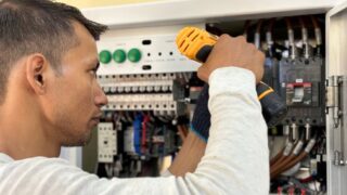 Professional electrician using a drill on an indoor circuit breaker panel.