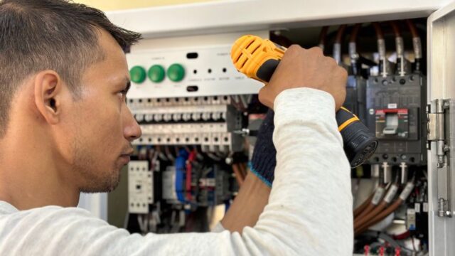 Professional electrician using a drill on an indoor circuit breaker panel.