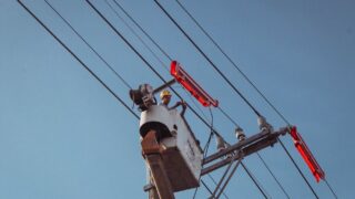 Electrician in a lift repairing overhead power lines on a clear day.