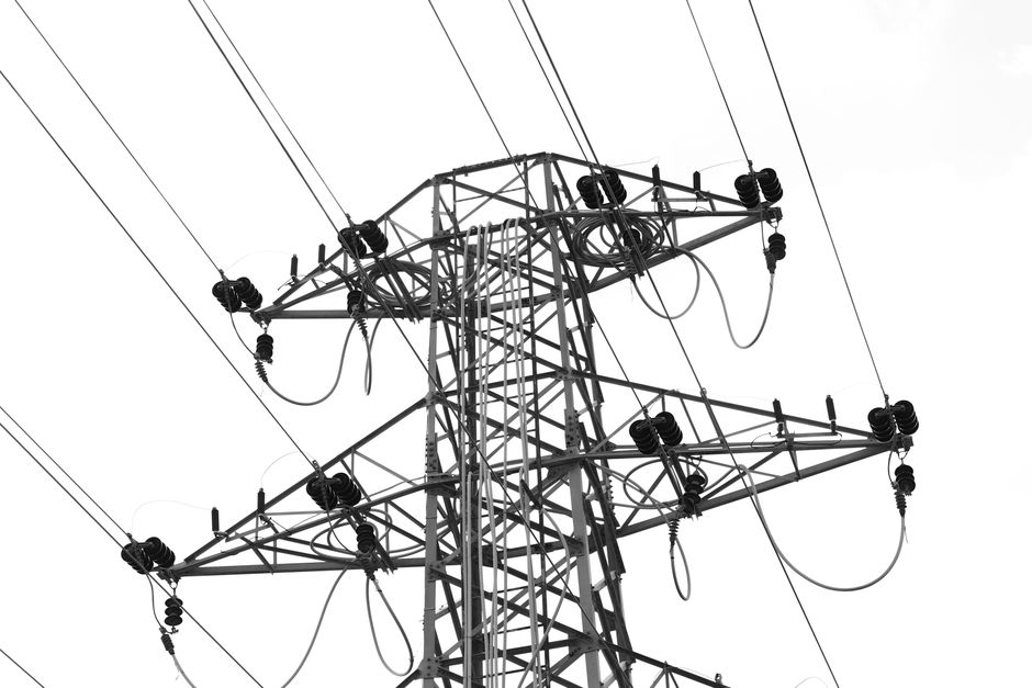 Black and white photo of high voltage power lines and electrical tower against a clear sky.