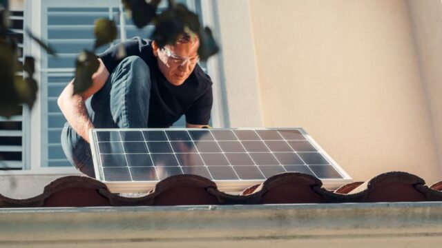 A technician installs a solar panel on a house roof, embracing clean energy solutions.