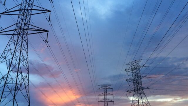 A scenic view of high voltage power lines silhouetted against a vibrant sunset sky.